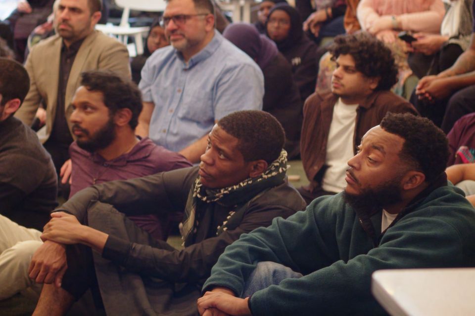 People seated close together indoors, turned toward a speaker out of frame.